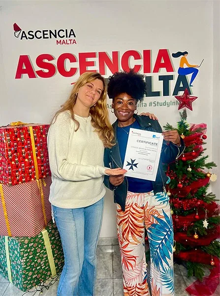 Student proudly holding certificate at Ascencia Malta with festive background